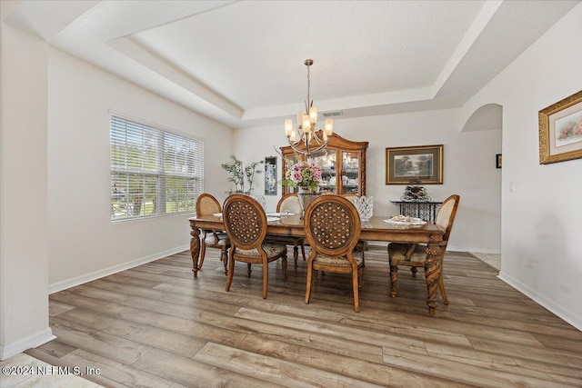 dining room featuring arched walkways, a raised ceiling, and wood finished floors