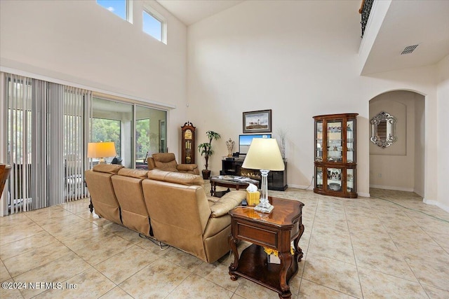 living room with arched walkways, visible vents, a high ceiling, light tile patterned flooring, and baseboards