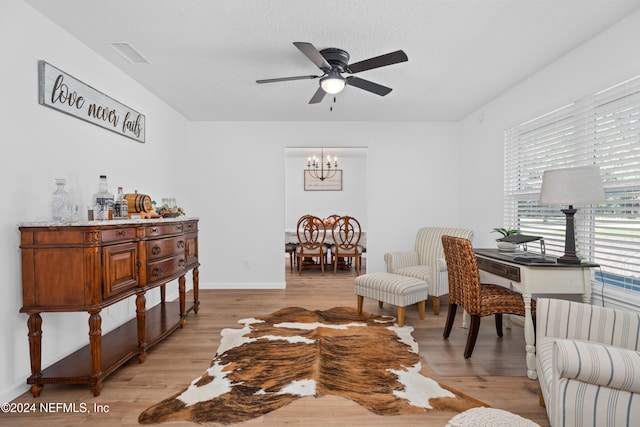 living room with a textured ceiling, light hardwood / wood-style floors, and ceiling fan with notable chandelier