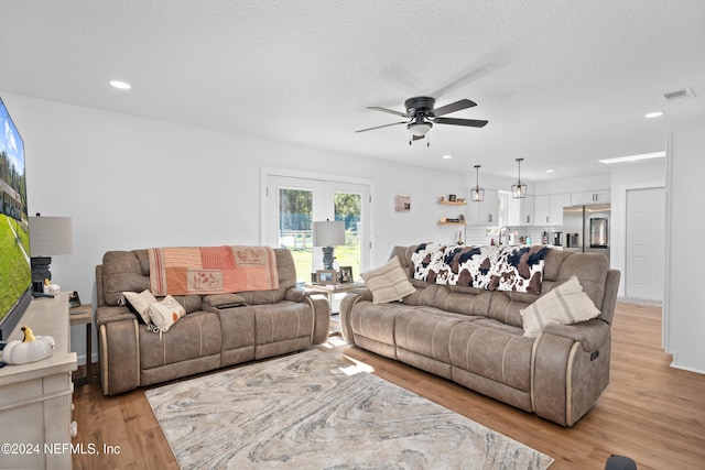 living room featuring ceiling fan, light hardwood / wood-style flooring, and a textured ceiling