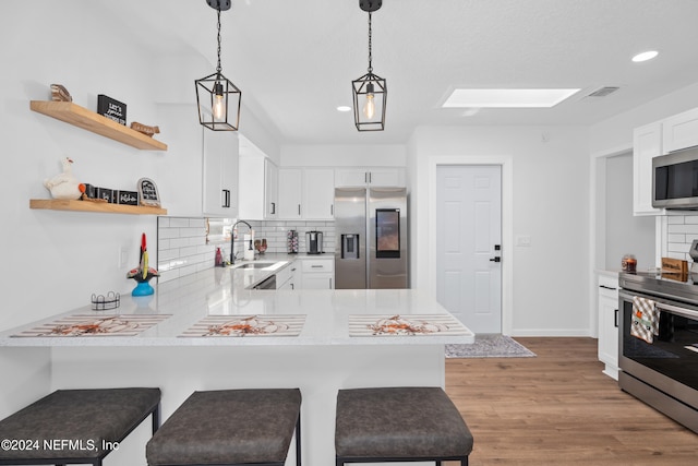 kitchen featuring white cabinets, light wood-type flooring, a kitchen bar, kitchen peninsula, and stainless steel appliances