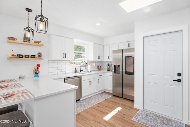 kitchen with kitchen peninsula, sink, light wood-type flooring, appliances with stainless steel finishes, and white cabinetry