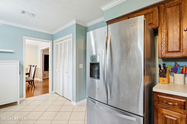 kitchen featuring stainless steel fridge, light tile patterned flooring, a textured ceiling, and ornamental molding