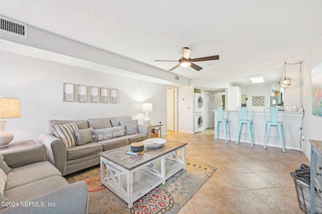 tiled living room with a textured ceiling, ceiling fan, and stacked washer / drying machine