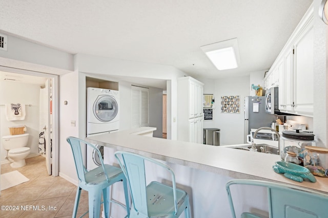 kitchen with stainless steel appliances, white cabinets, kitchen peninsula, light tile patterned flooring, and stacked washer and clothes dryer