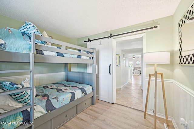 bedroom with a barn door, light hardwood / wood-style floors, and a textured ceiling