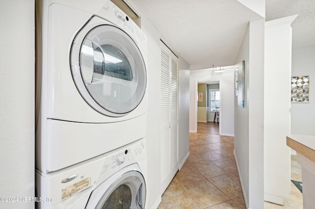 laundry room featuring a textured ceiling, light tile patterned flooring, and stacked washer and clothes dryer