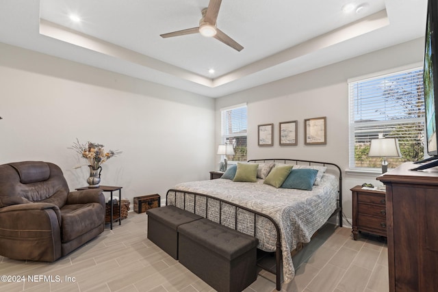 bedroom featuring a tray ceiling, multiple windows, and ceiling fan