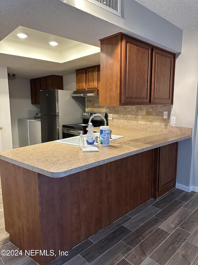 kitchen featuring a raised ceiling, kitchen peninsula, stainless steel appliances, and washing machine and clothes dryer