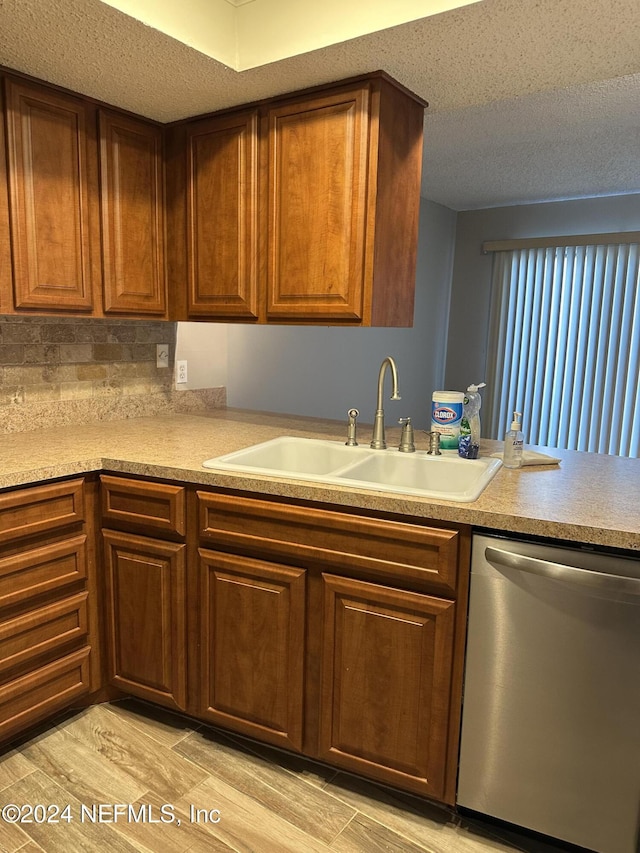 kitchen featuring light wood-type flooring, tasteful backsplash, a textured ceiling, sink, and dishwasher