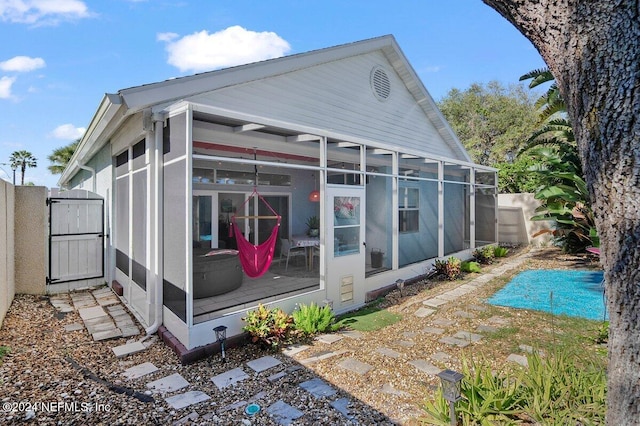 rear view of property with a sunroom, fence, and a gate