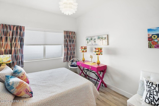 bedroom with light wood finished floors, an inviting chandelier, and baseboards