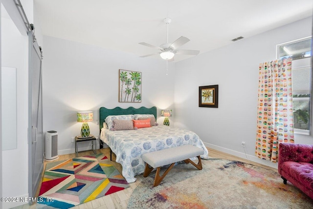 bedroom with a barn door, visible vents, baseboards, and wood finished floors