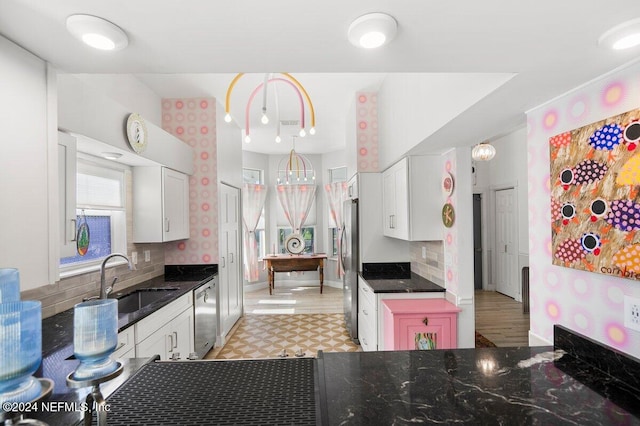 kitchen featuring baseboards, white cabinets, stainless steel appliances, pendant lighting, and a sink