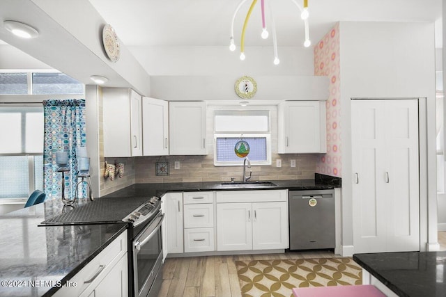 kitchen with white cabinets, dark stone countertops, a sink, stainless steel appliances, and backsplash