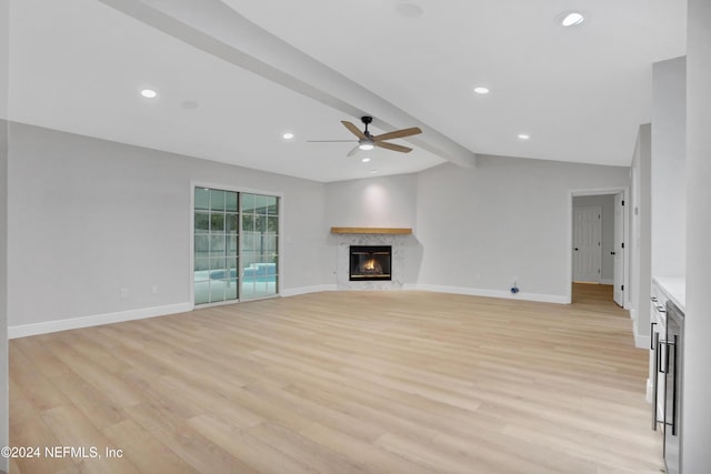 unfurnished living room featuring lofted ceiling with beams, light hardwood / wood-style floors, a fireplace, and ceiling fan