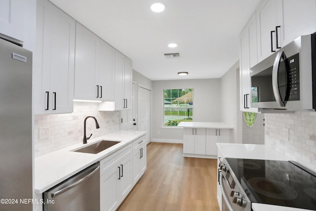 kitchen featuring backsplash, white cabinets, sink, light hardwood / wood-style floors, and stainless steel appliances