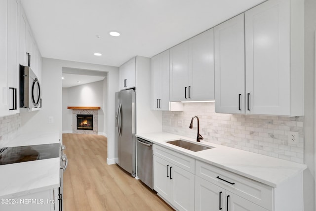 kitchen with sink, light stone counters, light hardwood / wood-style flooring, white cabinets, and appliances with stainless steel finishes