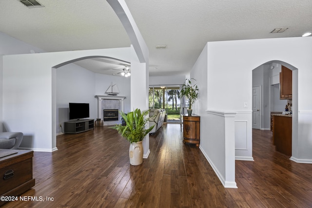 living room featuring a textured ceiling, ceiling fan, dark wood-type flooring, and a tiled fireplace