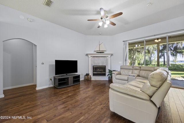 living room with a tile fireplace, a textured ceiling, dark hardwood / wood-style flooring, and ceiling fan