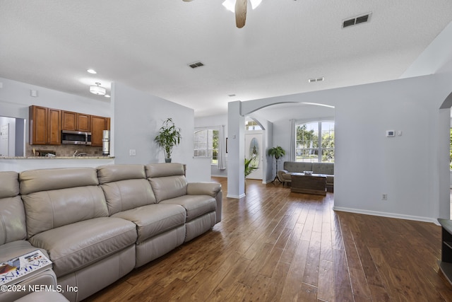 living room featuring ceiling fan, dark wood-type flooring, and a textured ceiling