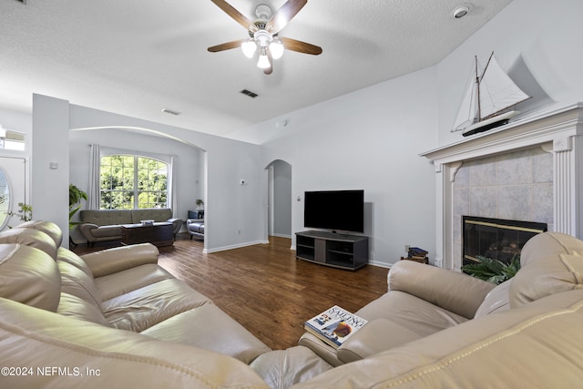 living room featuring lofted ceiling, a tile fireplace, dark hardwood / wood-style floors, ceiling fan, and a textured ceiling