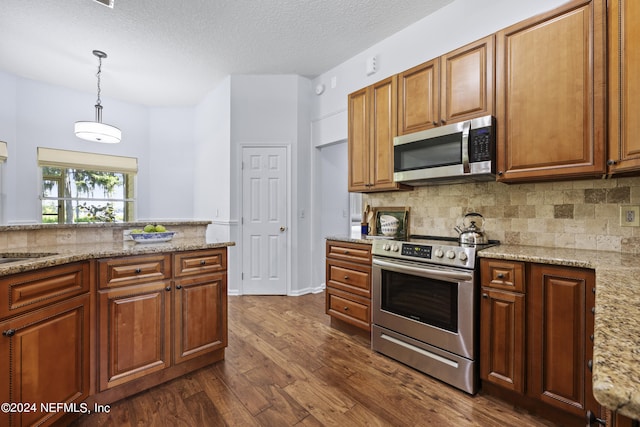 kitchen with pendant lighting, dark hardwood / wood-style flooring, light stone counters, and appliances with stainless steel finishes