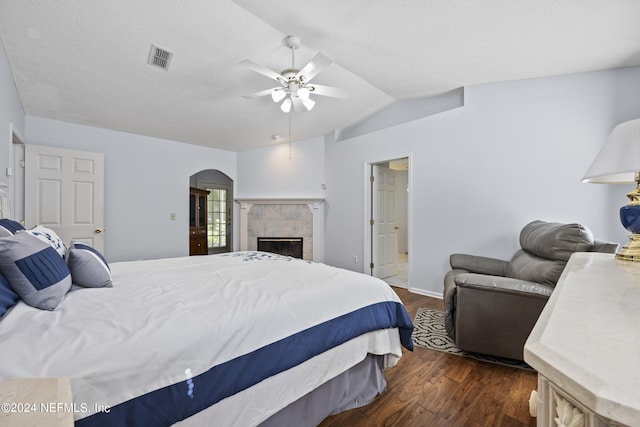 bedroom featuring a textured ceiling, ceiling fan, dark wood-type flooring, a fireplace, and lofted ceiling