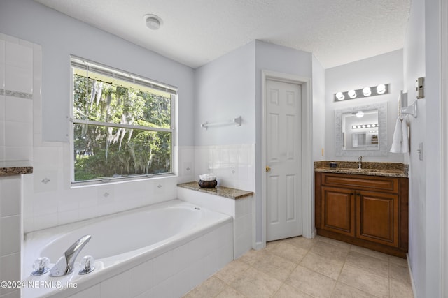 bathroom featuring tile patterned floors, vanity, a textured ceiling, and tiled bath