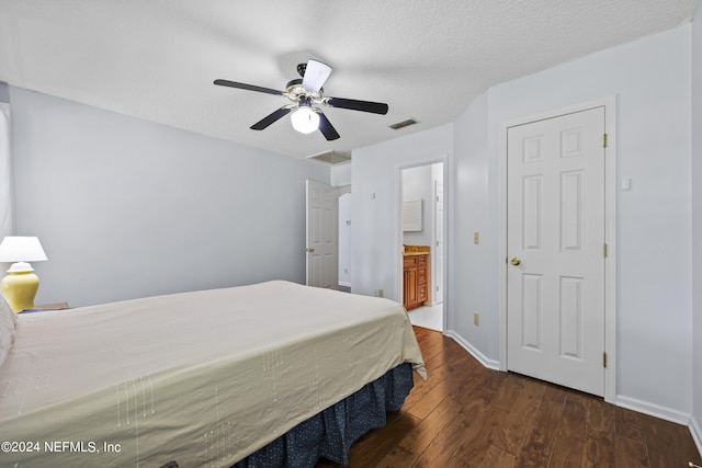 bedroom with a textured ceiling, ceiling fan, ensuite bathroom, and dark wood-type flooring