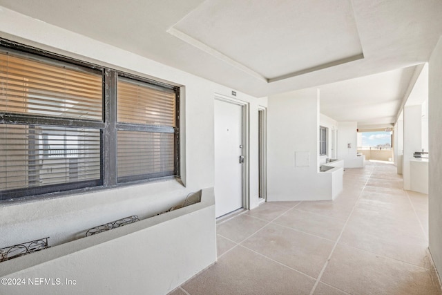 hall featuring a raised ceiling and light tile patterned flooring