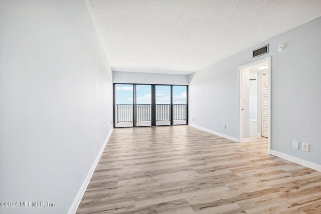 unfurnished room with light wood-type flooring and a textured ceiling