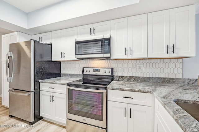 kitchen with light stone counters, light hardwood / wood-style floors, decorative backsplash, white cabinets, and appliances with stainless steel finishes