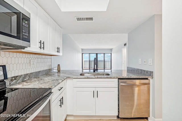 kitchen featuring white cabinets, sink, light stone counters, kitchen peninsula, and stainless steel appliances