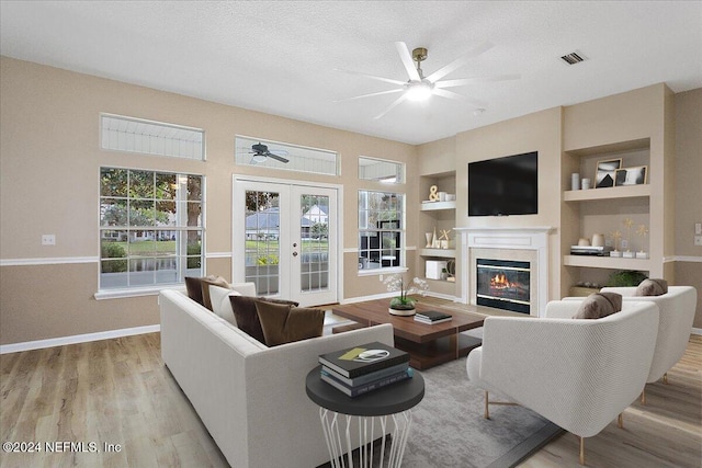 living room with french doors, light wood-type flooring, a textured ceiling, and built in features