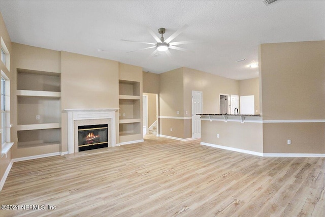 unfurnished living room with light wood-type flooring, a textured ceiling, ceiling fan, sink, and built in features