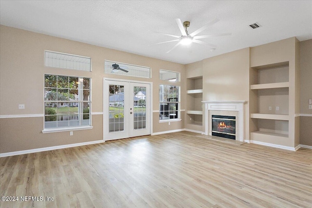 unfurnished living room with light wood-type flooring, built in features, a textured ceiling, and french doors