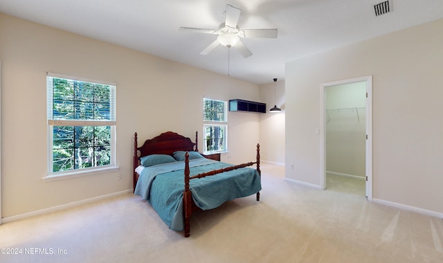 bedroom with a closet, a walk in closet, light colored carpet, and ceiling fan