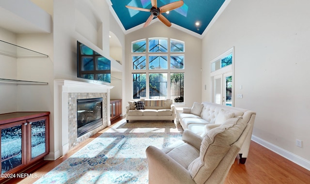 living room with ceiling fan, crown molding, wood-type flooring, high vaulted ceiling, and a fireplace