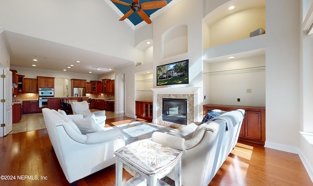 living room featuring ceiling fan, a high ceiling, hardwood / wood-style flooring, a fireplace, and ornamental molding