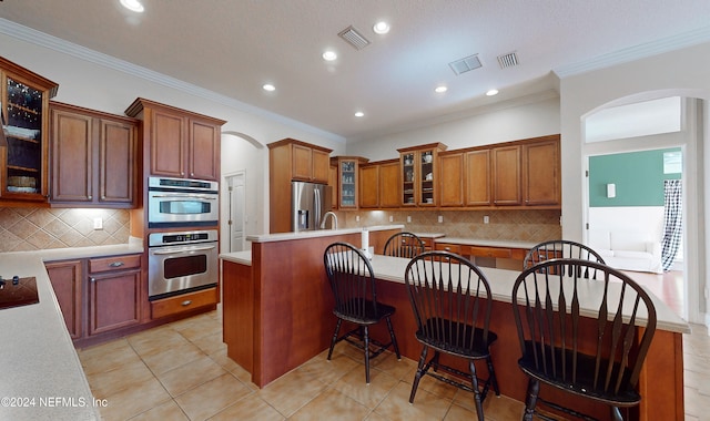 kitchen with a center island, stainless steel appliances, crown molding, a kitchen bar, and light tile patterned flooring