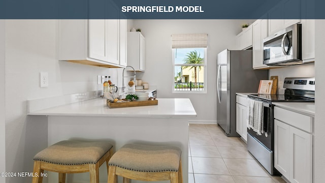 kitchen with kitchen peninsula, a kitchen breakfast bar, stainless steel appliances, white cabinetry, and light tile patterned flooring