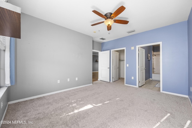 unfurnished bedroom with ceiling fan, light colored carpet, a walk in closet, and connected bathroom