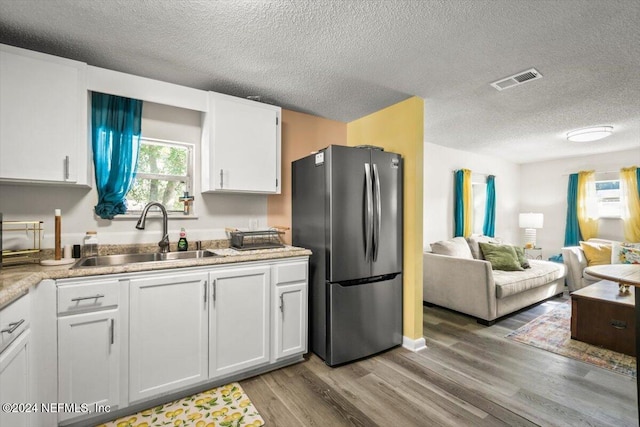 kitchen with sink, light wood-type flooring, a textured ceiling, white cabinetry, and stainless steel refrigerator