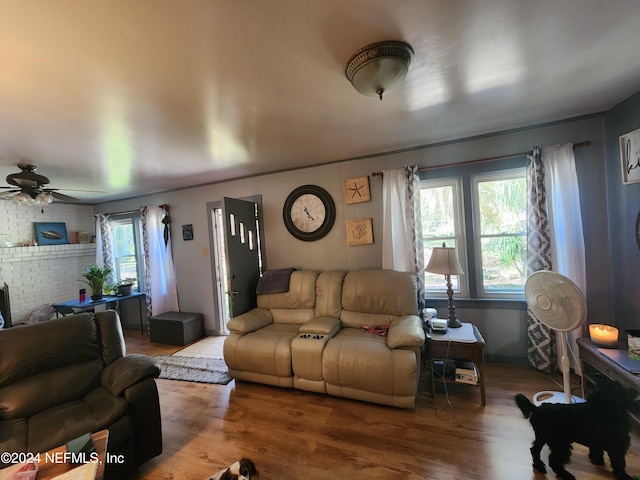 living room featuring hardwood / wood-style flooring, ceiling fan, and brick wall