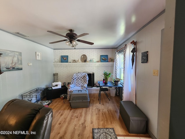 living room with ceiling fan, light hardwood / wood-style floors, ornamental molding, and brick wall