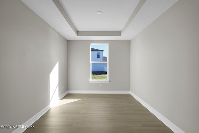 spare room with a tray ceiling and dark wood-type flooring