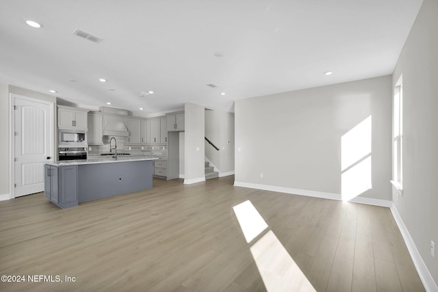 kitchen with light hardwood / wood-style flooring, backsplash, gray cabinets, a center island with sink, and white microwave