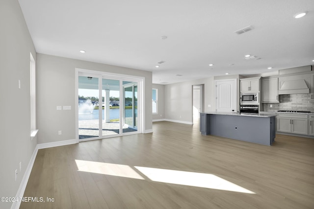 kitchen with backsplash, a kitchen island with sink, a water view, light wood-type flooring, and appliances with stainless steel finishes