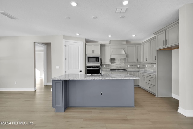 kitchen with appliances with stainless steel finishes, a kitchen island with sink, gray cabinetry, and custom exhaust hood